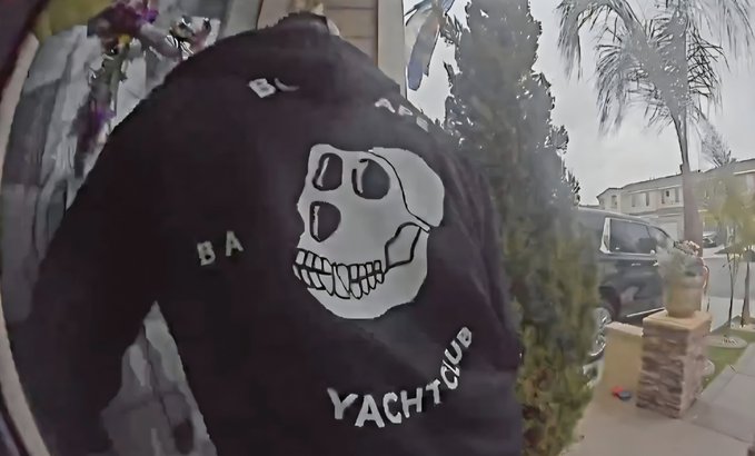 A security camera view of a front porch showing a black jacket with a skull design and the words 'BLACK FLAG BABY YACHT CLUB' printed on it.
