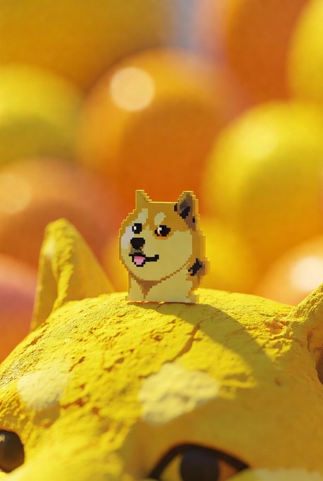 A small pixel-art Shiba Inu figurine stands on a yellow textured surface against a blurred golden background.