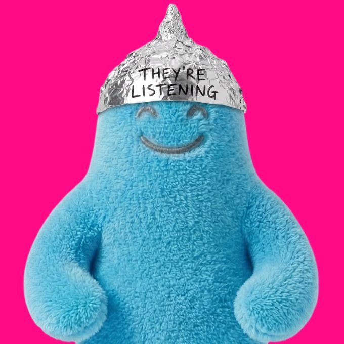 A fluffy blue character with a smiley face wears a tin foil hat labeled "THEY'RE LISTENING" against a hot pink background. The image serves as the user's profile picture, with the conspiracy-themed hat symbolizing their origin story and passion being reawakened by the GBOY NFT collection.