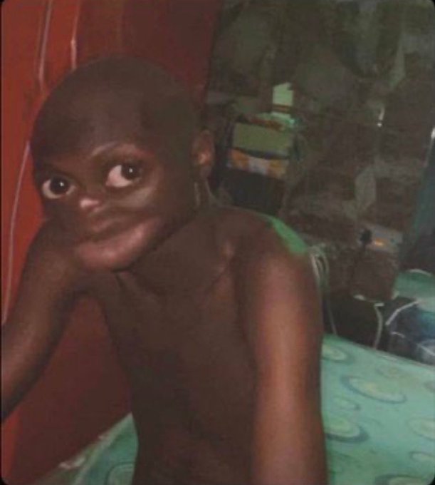 A young, shirtless child with dark skin looking back over their shoulder in a dimly lit room.