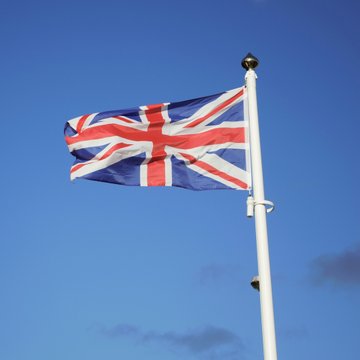 The Union Jack flag waves against a clear blue sky, symbolizing the United Kingdom's jurisdiction where a court recently ordered two men behind a £1.5M crypto investment fraud to repay victims £851,402 following an FCA prosecution.