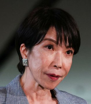 The image shows a middle-aged woman with short dark hair wearing a checkered blazer and a small square silver earring, with a slight smile and teary eyes suggesting an emotional moment. The "OMG" caption relates to the image by expressing astonishment, possibly at her emotional reaction or something significant she just heard or witnessed.