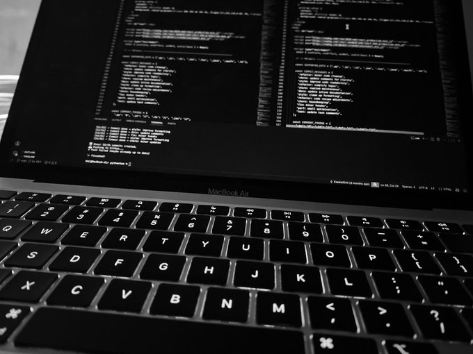 A close-up, black-and-white view of a MacBook Air keyboard with lines of code visible on the screen.