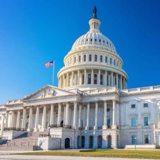 The U.S. Capitol Building stands prominently under a clear blue sky with the American flag flying, symbolizing the legislative urgency behind Senator Lummis's warning that Congress must act quickly on the Clarity Act despite numerous proposed changes.