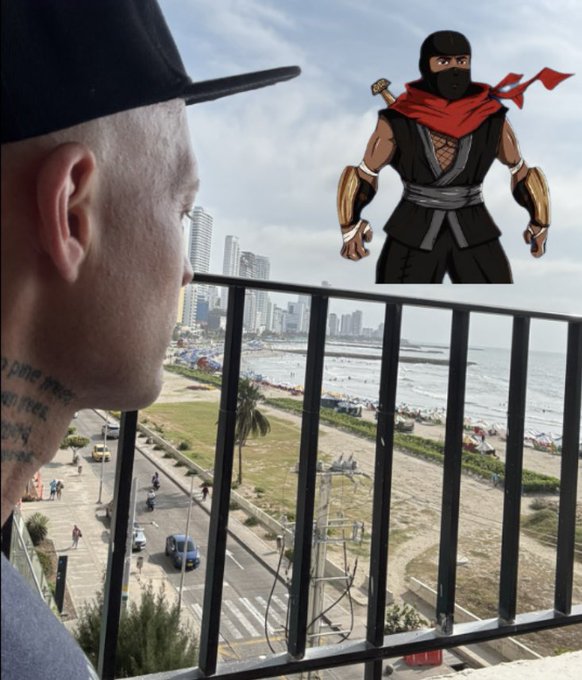 A photo of a man in a black cap looking out from a balcony at a coastal city scene, with an animated Mortal Kombat-style ninja character superimposed in the sky.