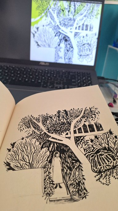An open sketchbook rests in front of a laptop displaying a digital drawing; the sketchbook features a detailed black-and-white illustration of a person under a large tree.