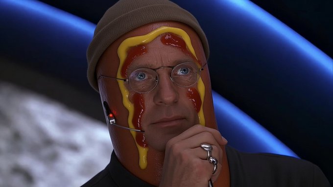A meme image showing a man wearing a hot dog costume and a beanie, with ketchup and mustard drawn on his face, looking thoughtfully off-camera. The post's request to "run the coin to $1.50" pairs humorously with the image, as the man's serious, contemplative expression suggests he's "calculating" the perfect recipe or strategy—mirroring how traders might be weighing their next move.
