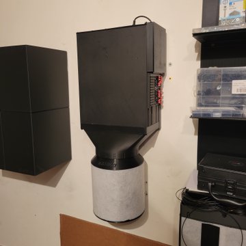 The image shows a small, black air purification unit mounted on a wall next to some shelves with various items on them. The air purifier has been repurposed as an air filter for these slim units, which are placed against the wall. This creative use of the air purifier demonstrates how everyday objects can be adapted and repurposed for different needs or situations.