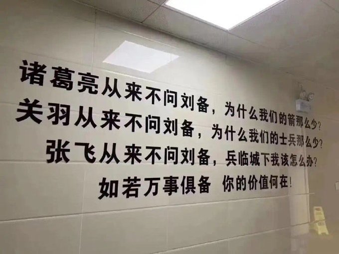 Black Chinese characters mounted on a white tiled wall read a motivational message about Zhuge Liang, Guan Yu, and Zhang Fei never asking Liu Bei about resources, questioning one's value when everything is prepared.