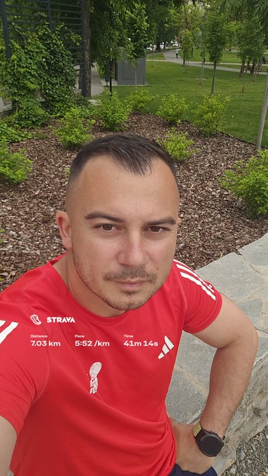 A man in a red Adidas shirt takes a selfie after completing a 7.03 km run with a 5:52/km pace in 41m 14s, displayed on a Strava overlay. The image, captioned "Evening run with #STEPN at 29 degrees," shows him outdoors in a park setting, with the activation code 93710171 mentioned for the STEPN run-to-earn app.