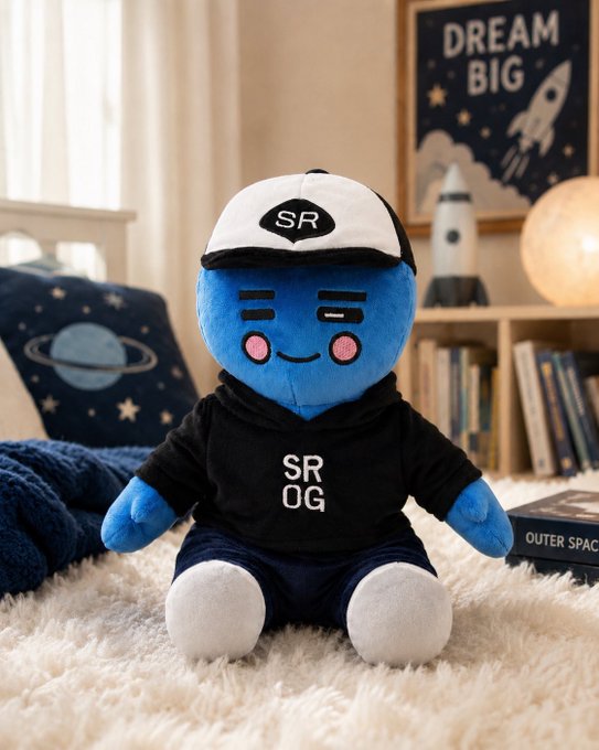 A blue plush toy character wearing a black and white 'SR' cap and an 'SRO OG' hoodie, sitting on a fluffy white rug in a room with space-themed decor including a 'DREAM BIG' poster and a rocket toy.