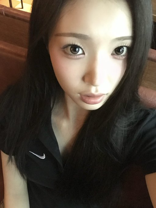 A young woman with long dark hair and dramatic eye makeup wears a black Nike polo shirt, taking a close-up selfie.
