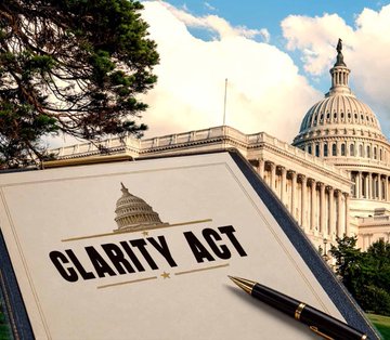 A bound document labeled "CLARITY ACT" sits on a desk with a fountain pen, set against the backdrop of the U.S. Capitol building, visually reinforcing the post's message about Charles Schwab's support for the Crypto Clarity Act and the push for crypto regulation in Congress.