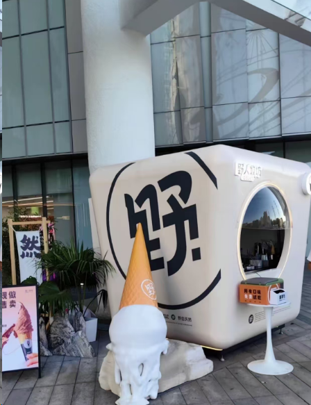An oversized ice cream mascot sculpture with a melting cone stands in front of a building decorated with the large Chinese character '嗨' (Hi).