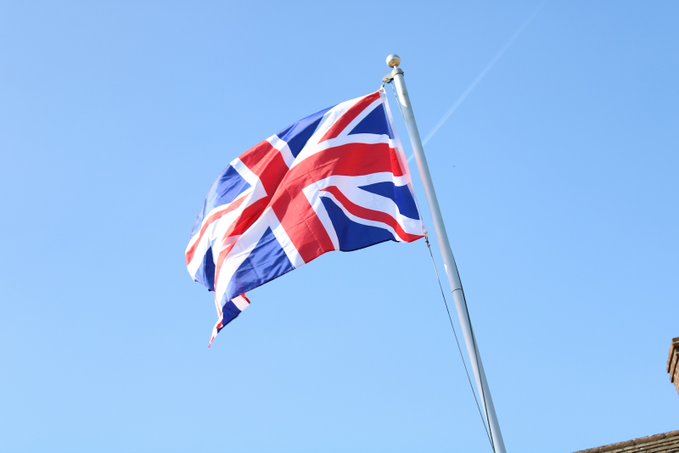 The Union Jack flies against a clear blue sky, representing the United Kingdom. This relates to the FCA's discussions with banks regarding tokenized gold regulations in the UK wholesale markets.