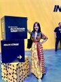 An event stage with a yellow backdrop where a woman in a floral dress stands beside a blue 'MULTICHAIN' podium, partially showing 'IN' text behind her.