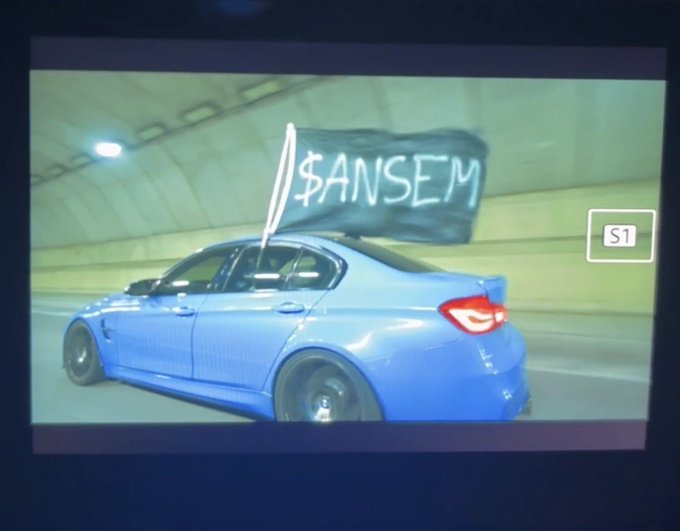 A blue BMW sedan speeds through a tunnel with a black flag displaying "$ANSEM" waving from its window, paired with a "banger loading..." caption that visually reinforces the imminent arrival of hype-filled content from the trader Ansem.
