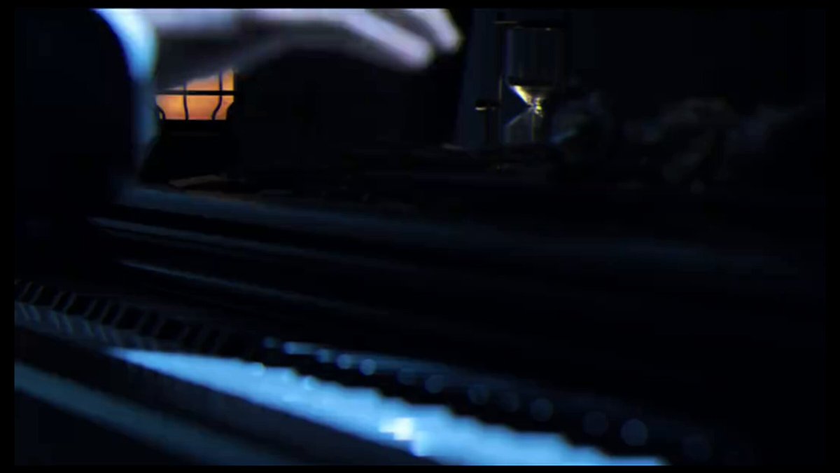The image shows a person's hand holding an hourglass with sand inside of it, which appears to be lit up against a dark background. The scene takes place next to a keyboard, suggesting that this might be a music performance or a video game setting. The focus on the hourglass and its illumination in the darkness indicates that the image is likely related to a time-sensitive event or situation, possibly involving finance or gaming elements.