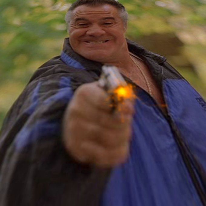 A muscular man with gray hair in a blue and black jacket grins menacingly while firing a gun directly at the camera, with a bright muzzle flash illuminating the barrel. The image's aggressive, confrontational pose visually reinforces the "$Gunner anti-thesis" theme, suggesting a defiant counter-narrative or opposition stance to the gun-related token.
