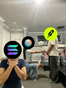 Three people pose in a modern living room with their faces obscured by logos: a woman in a dark blue shirt covers her face (likely representing a betrayed ally), a person in the middle holds a colorful orb-like logo, and a standing person wears the green Solana logo, all set against a cozy home interior with a couch and kitchen visible in the background.