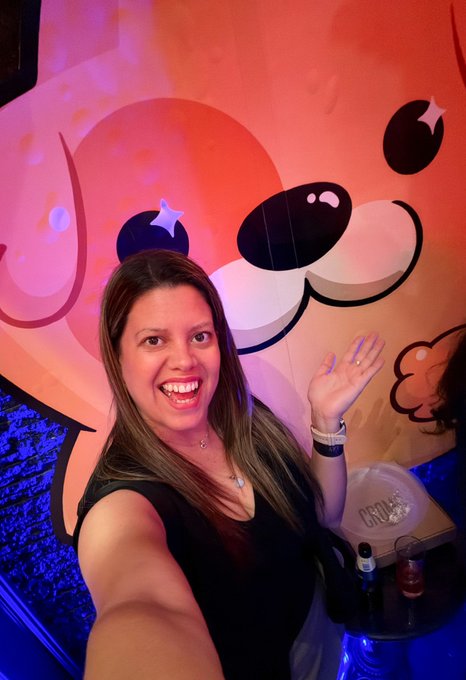The image features a woman taking a selfie with her phone, capturing herself wearing a black dress against an orange background that resembles a cartoon dog's face. The caption of the photo includes the words "Kanstar secret party" and "@KanstarWorld @Ronin_Network". This suggests that the woman is attending or has attended a party where the theme was a cartoon dog, possibly at a Kanstar World event.

The image also contains several bottles scattered around her, which could be related to the party or simply decorations for the photo session. The presence of these items and the context of the post indicate that this might be an event related to the Kanstar Secret Party or similar social gathering.