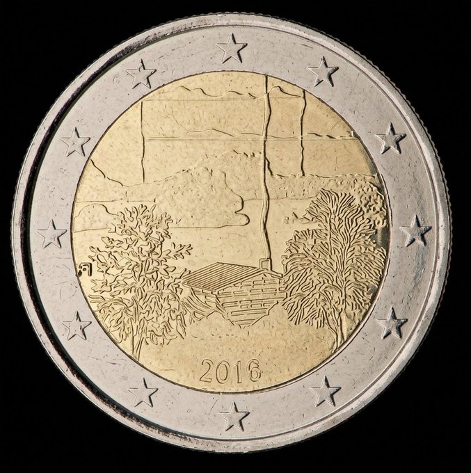 A close-up of a 2016 bimetallic coin displaying a landscape scene with trees and mountains on its golden center.