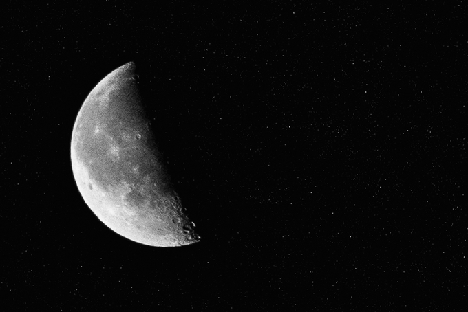 A black and white photograph of a crescent moon set against a dark, star-speckled night sky.