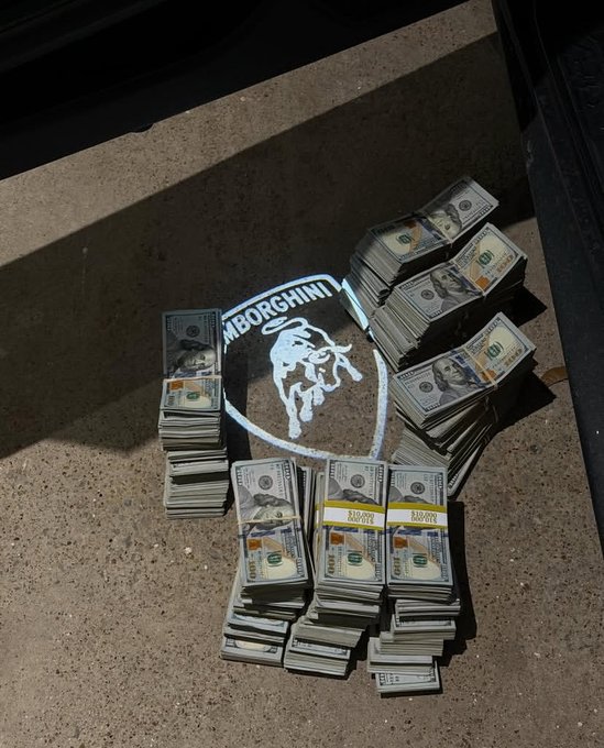 Multiple banded stacks of $100 bills are arranged in a circle around a Lamborghini logo projected onto concrete, visually connecting the "No Risk, No Lambo" mantra with the tangible cash needed to afford the luxury vehicle.