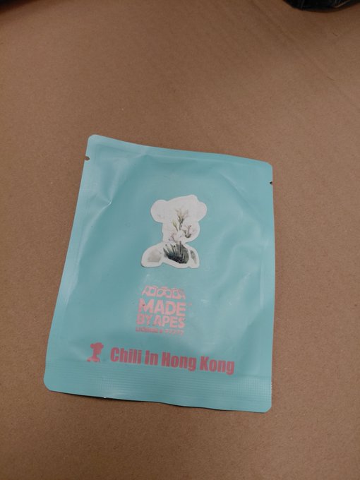 A light blue foil pouch labeled 'made by apes' and 'Chili In Hong Kong' resting on a tan surface, featuring a bear-shaped illustration with a plant.