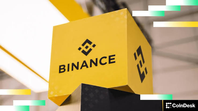A CoinDesk image showing a yellow cube displaying the Binance logo and name, with Binance's signature geometric symbol visible on multiple sides.
