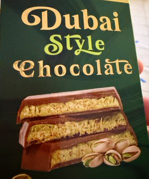 The image shows a "Dubai Style Chocolate" package with a picture of a chocolate bar filled with pistachio and what appears to be shredded phyllo or crispy filling. The caption "Feeling scammed" humorously suggests that the actual chocolate likely didn't match the generous, picture-perfect filling shown on the packaging, a common consumer complaint about misleading product imagery.