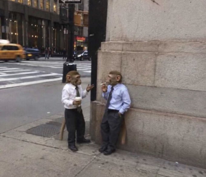 Two figures wearing monkey masks, dressed in business attire (white shirts, ties, and slacks), stand on a city street corner taking a smoke break, with a yellow taxi visible in the background. The image humorously conveys a "monkey see, monkey do" sentiment about financial markets, fitting the post's message to "have a great week" as a tongue-in-cheek commentary on the unpredictable, herd-like nature of trading in GM and CT stocks.