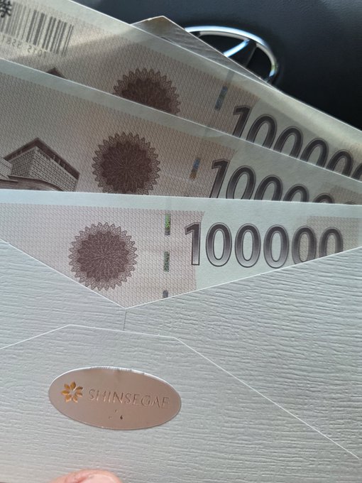Three envelopes containing vouchers labeled '1000000' rest on a textured folder branded 'SHINSEGAE', taken inside a vehicle.