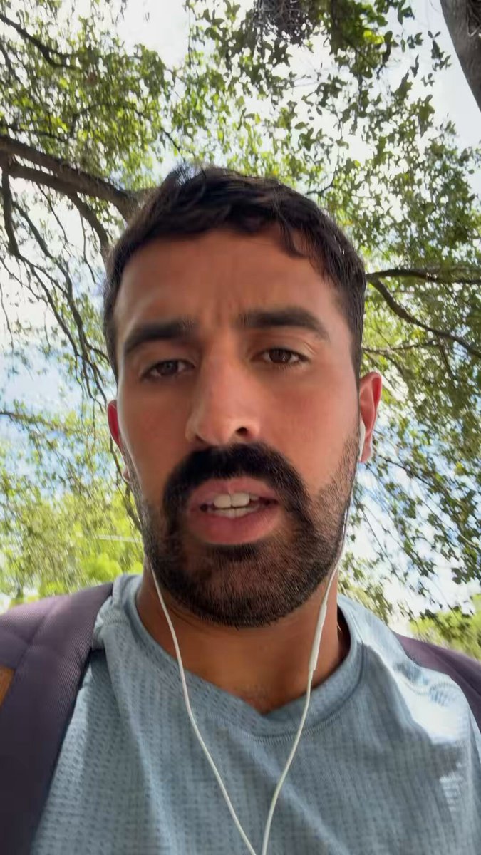 In this image, there's a man with a beard wearing headphones who looks down at his phone while standing outdoors underneath trees. The photograph depicts a person engaging in an online discussion or conversation about cryptocurrency, as suggested by the presence of a text overlay that says "Clemente thinks it’s impossible for sol to ever make a new ATH sol is running into the same issue as eth where success of the network does not equal token price go up". The man's expression and surroundings indicate his interest in this topic.