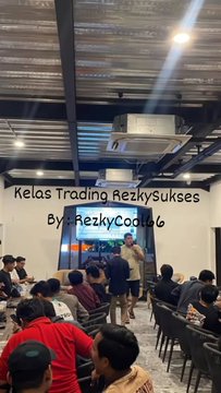 A trading class called 'Kelas Trading RezkySukses By RezkyCoin96' held in a warehouse-style venue, with attendees seated and an instructor standing at the front.