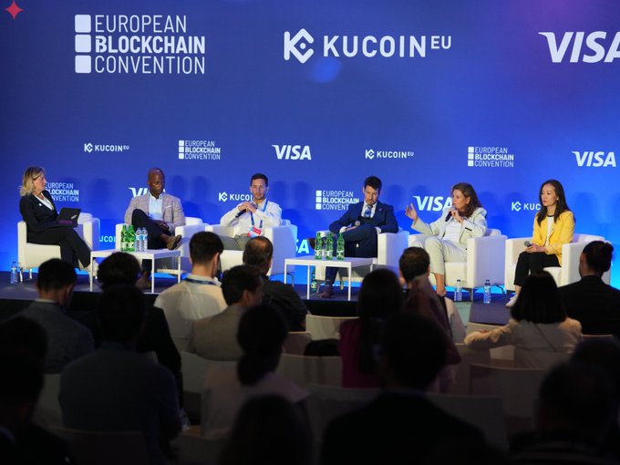 A panel discussion at the European Blockchain Convention, featuring speakers seated on stage with KuCoin EU and Visa branding visible on the backdrop.