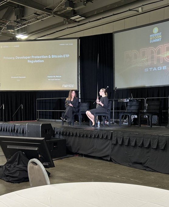A photograph of two women seated on stage at the 'Midwest Bitcoin Summit' discussing 'Privacy, Developer Protection & Bitcoin ETP Regulation', with speakers Elizabeth Hempowicz and Heather M. Plushke.