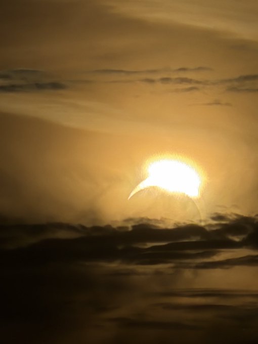 A golden sun rises through a hazy, amber-toned sky, partially obscured by wispy clouds near the horizon.