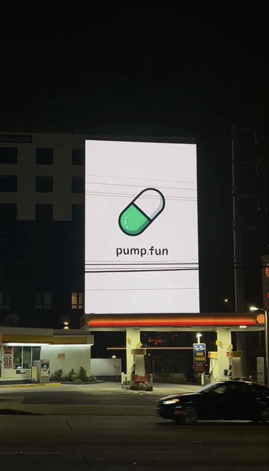 A nighttime photograph of a large illuminated billboard displaying the 'pump.fun' logo (a green and white pill/capsule icon) above a gas station.