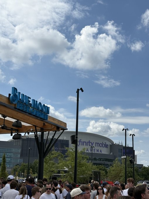 A crowd gathers outside the 'BLUE MOON' beer garden near the Xfinity Mobile Arena under a partly cloudy sky.