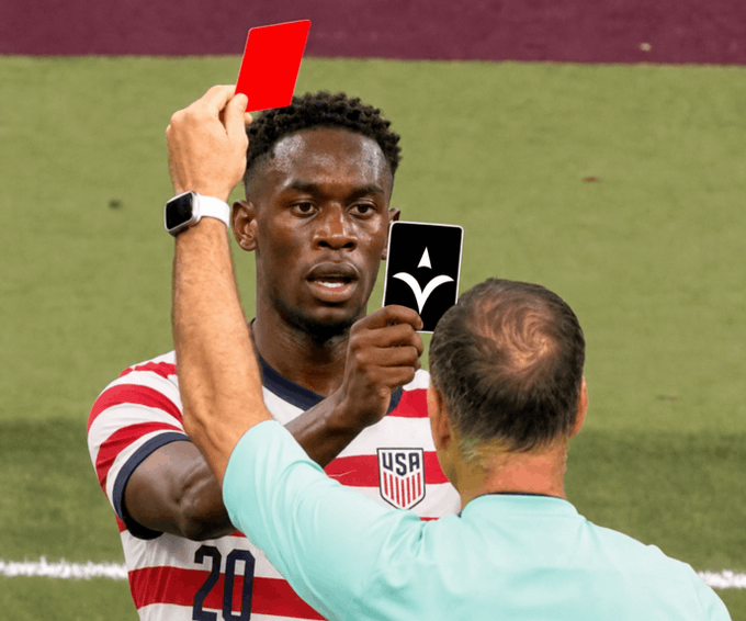 A US soccer player wearing jersey number 20 receives a red card from a referee during a match.