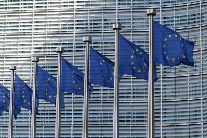 A row of European Union flags flies against the glass facade of an EU institutional building, symbolizing the regulatory authority behind the MiCA framework that Circle's head of EU policy Patrick Hansen is urging to adopt an equivalence rule for foreign stablecoin issuers.