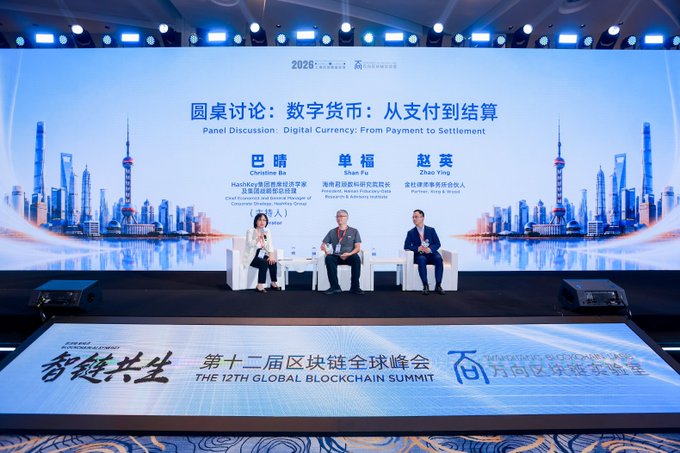 A panel discussion titled 'Digital Currency: From Payment to Settlement' at the 12th Global Blockchain Summit, featuring three speakers on stage with a Shanghai skyline backdrop.
