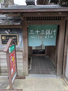 A traditional Japanese building houses a "Sanju San Ginkō" (Thirty-Three Bank) ATM, its elegant noren curtain and wooden entrance exuding refined, old-world charm.

The image illustrates the post's point by showing how a bank can blend cultural tradition with modern finance—just as JPYC, already operating as a bank, could pair its digital services with touches like New Year's fortunes to achieve similar elegance.