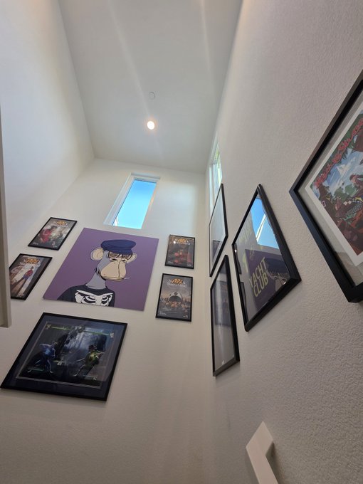 An interior view looking up a staircase at a wall decorated with framed movie posters and a large purple artwork of a cartoon cat character.