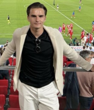 A man with slicked-back hair, wearing a beige blazer over a black shirt with sunglasses tucked into the collar, poses at a football stadium during a match, seemingly posing as a "man of the people" amid the playful commentary about market cycles and misplaced blame.