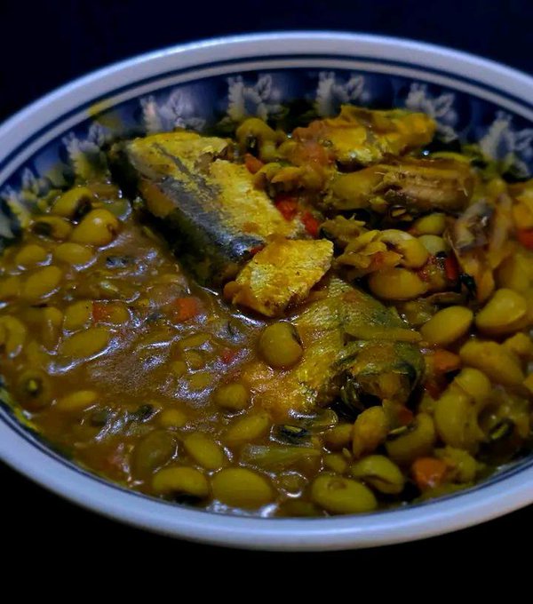 A bowl of stew with green peas and a piece of fish, possibly mackerel, in a patterned bowl.