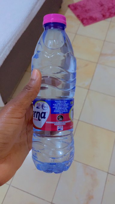 A hand holding a clear plastic water bottle with a pink cap and a label that appears to read "Tana" with some Japanese text.