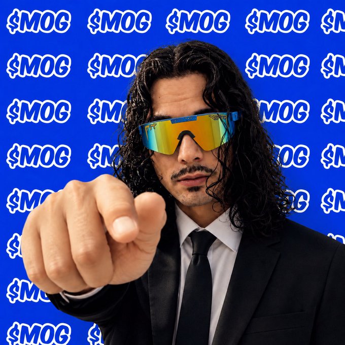 A man with long curly hair wearing reflective sunglasses and a black suit points directly at the camera, set against a bright blue background covered with '$MOG' logos.