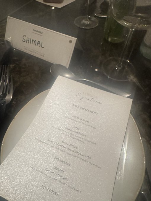 A 7-course "Signature" set menu from Shima at The Founders Table is displayed on a white plate, featuring dishes like Spinach Mado Maki, Sous Vide Charcoal Grill Steak, and Roasted Coconut Meringue. A reserved name card for "SHIMAL" sits beside the menu, complementing the post's celebration of fine dining funded by @FundedXyz.